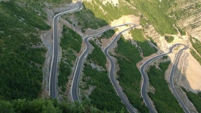 Drone view of epic roads in the north albanian mountains, famous curves and hairpin turns of SH20 road above the Cem river gorge in morning. Sun is just rising over the mountains.