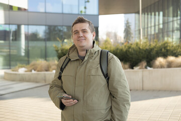 Handsome young man using phone outdoor. Smiling businessman walking outdoors using mobile in urban...