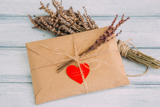 Close-up of a brown Envelope sealed with a heart sticker, brown string and decorated with dried flowers on a wooden table