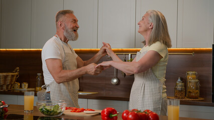 Romantic senior retired Caucasian family couple dancing waltz celebrate marriage anniversary cooking dinner old husband spin mid-aged wife in dance listen music at kitchen happy woman and man have fun