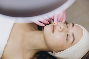 Beautician injecting hyaluronic acid lip filler into patient's lips for lip augmentation and face...