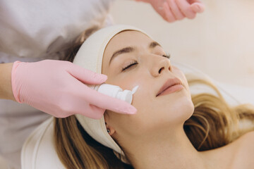 Beauty professional applying moisturizing cream on relaxed female client during facial skincare procedure in spa setting