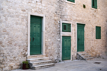Vibrant green doors stand out against the textured stone walls of a peaceful coastal town. The afternoon light casts gentle shadows, enhancing the tranquil atmosphere.