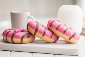Sweet pink donut with chocolate strips on white table.