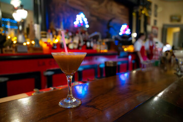 A frozen daiquiri in a cocktail glass with a straw, placed on the wooden bar counter of Floridita in Havana, Cuba, with a blurred festive background.  