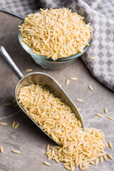 Orzo, kritharaki, risoni pasta. Uncooked dry pasta in scoop on kitchen table.