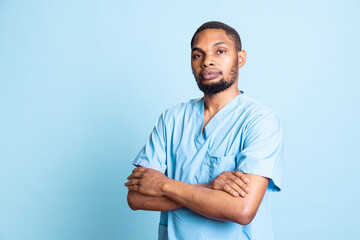 Portrait of upbeat african american medical staff standing with arms crossed, studio background. Radiant healthcare employee smiling, wearing protective clinical workwear on the job.