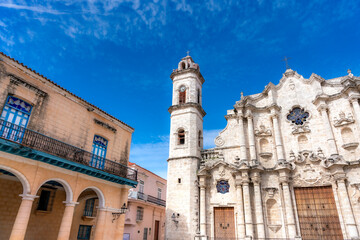 Fototapeta premium The Havana Cathedral, a stunning baroque church in Old Havana, Cuba, stands beside colonial buildings with arched balconies under a bright blue sky. 