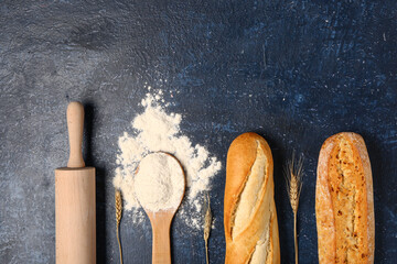 Composition with baguettes, flour, rolling pin and wheat ears on dark blue table