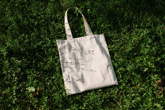 White cotton or mesh bag on green branches of a coniferous bush background. Zero waste, no plastic, eco friendly shopping, recycling concept. Blank mockup shopper, place for text. copy space flat lay