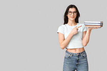 Young woman in eyeglasses pointing at books on grey background. Feminism concept