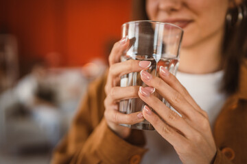 close up on woman hands stand and hold glass of water at home