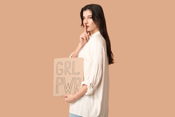 Young woman with sign GRL PWR showing silence gesture on beige background. Feminism concept