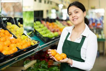 Female grocery store worker lays out ripe tangerines on the counter and display case