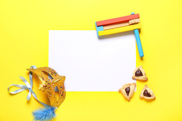 Composition with blank card, carnival mask, rattle and Hamantaschen cookies for Purim holiday on yellow background
