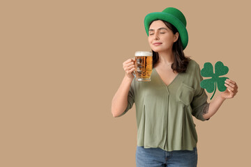 Beautiful young woman in leprechaun hat with glass of beer and clover on brown background. St....