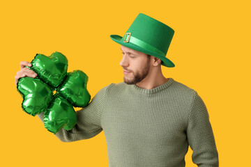 Young man in leprechaun hat with air balloon in shape of clover on yellow background. St. Patrick's...