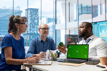 Mature couple attend a consultation with a financial broker about retirement plans, using isolated mockup screen on laptop. Specialist and clients covering savings growth and financial security.