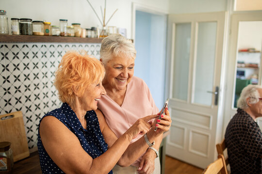 Senior women taking selfie together in kitchen laughing