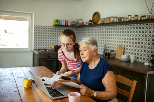 Granddaughter helping grandmother with medication instructions at home kitchen table