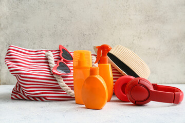 Composition with bottles of sunscreen cream, headphones, bag, sunglasses and hat on white table near light wall