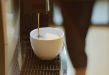 Turquoise cup pouring with two jets of hot coffee from beige espresso coffee machine pump. Close-up of coffeemaker. Coffee latte preparation.