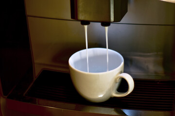 Turquoise cup pouring with two jets of hot coffee from beige espresso coffee machine pump. Close-up of coffeemaker. Coffee latte preparation.