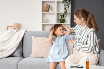 Mother combing her little daughter's hair with pediculosis on sofa at home
