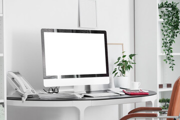 Workplace with blank computer monitor, telephone and plant in light office