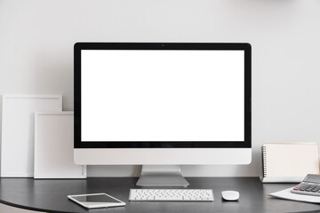 Fototapeta premium Blank computer monitor with frames on desk near light wall