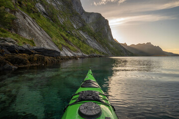 A green sea kayak on blue ocean water surrounded by mountains at sunset. 