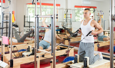 Young guy in sportswear training with straps in pilates studio