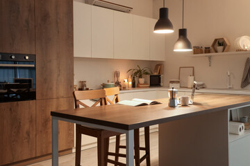 Interior of kitchen with table, counters and glowing lamps in evening