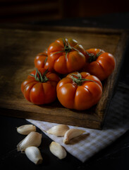 Pomodori rossi con aglio su tagliere in legno e sfondo scuro