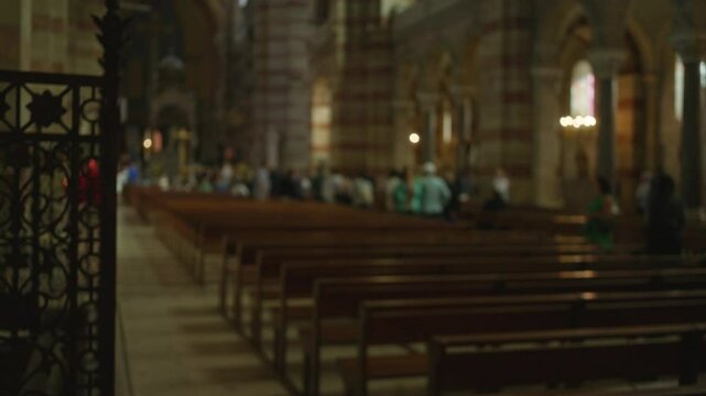 Blurry interior of a church with people milling around the benches under dim lighting, highlighting the architectural beauty of religious space indoors.