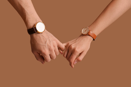 Couple with wristwatches holding pinkies on brown background