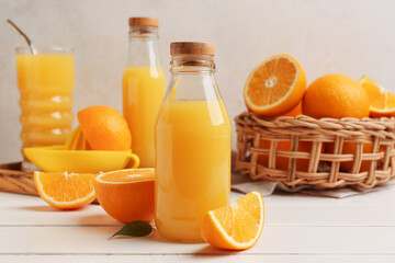 Glass bottle of tasty juice with oranges on white wooden table