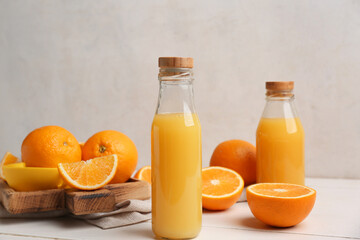 Oranges with juicer and glass bottles of tasty juice on white wooden table