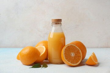 Oranges with glass bottle of tasty juice and leaves on light background