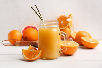 Mason jar of tasty juice and glass with oranges on white wooden table