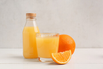 Oranges with glass and bottle of tasty juice on white wooden table
