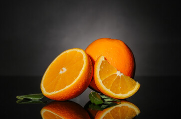 Tasty cut oranges with leaves on dark background