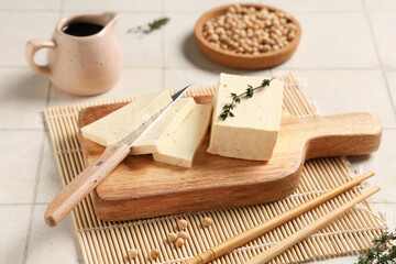 Board with tasty tofu cheese and knife on light tile background