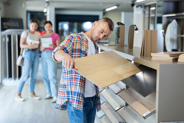 Interested casual young adult man thoughtfully evaluating eco-friendly wood grain laminate flooring...