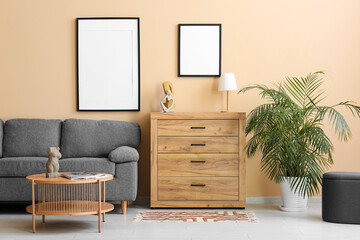 Chest of drawers, table and sofa near beige wall with hanging empty posters