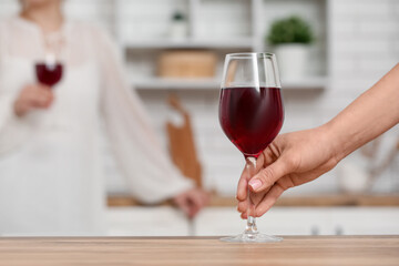 Hand of woman with glass of red wine in kitchen