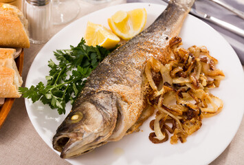 Baked branzino fish with vegetable garnish of grilled onion, slice of lemon and parsley