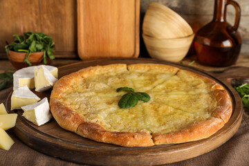 Wooden board with tasty pizza and  pieces of cheese on napkin
