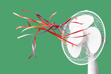 Modern electric fan with colorful fluttering ribbons on green background, closeup