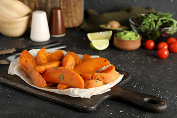 Wooden board with baked sweet potato on black grunge background